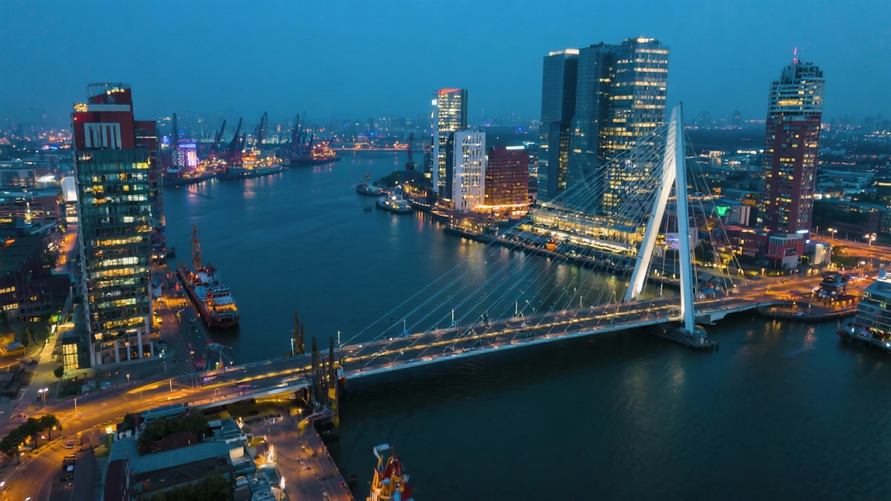 Evening aerial view of modern Rotterdam skyline with Erasmus Bridge and illuminated offices reflecting energetic digital marketing innovation near the bustling port.